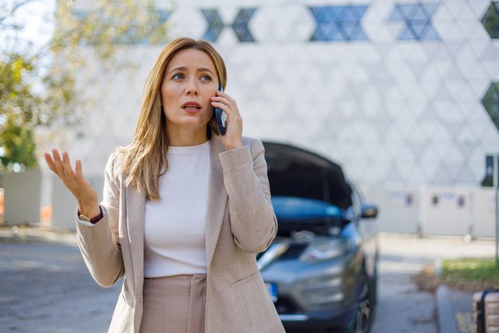 A vivid image of a displeased mid-adult woman standing by her damaged car, epitomizing the unforeseen challenges of road travel and the need for roadside assistance